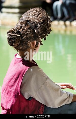 Coiffure romaine féminine complexe de classe supérieure portée par un réacteur féminin assis sur le bord du Grand bain, Bath, Angleterre. Copier l'espace. Vue arrière. Banque D'Images