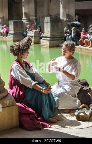 Deux femmes en costume romain assis sur le bord du Grand bain romain, Bath, Angleterre. Femmes réacteurs dans une conversation animée. Coiffure extrême Banque D'Images