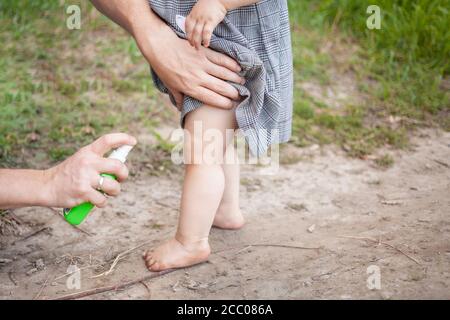 Papa traite sa fille avec un spray moustique. L'homme utilise du spray sur les bras et les jambes de l'enfant. Protection contre les moustiques dans la forêt. Vaporiser du mois Banque D'Images