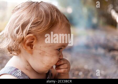 Bébé sale dans les bois. Une fille avec un visage sale creusait dans le sol et la suie. Portrait d'un enfant d'un an. Banque D'Images