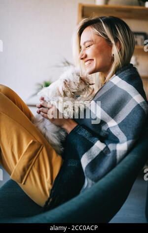 Belle femme jouant avec un chiot sur un canapé à la maison Banque D'Images