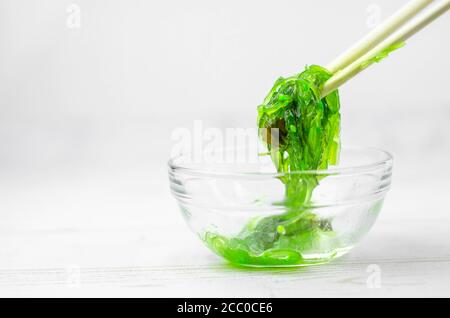 Salade d'algues wakame vertes dans des bols en verre transparent, sur une table en bois blanc Banque D'Images