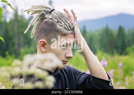 Portrait d'un jeune homme avec des dreadlocks sur toile de fond d'un parc forestier et de montagnes Banque D'Images