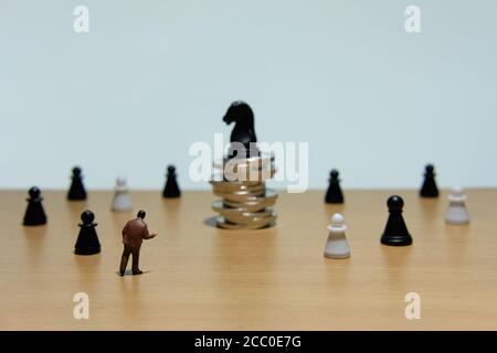 Photo conceptuelle de la stratégie d'affaires - homme d'affaires miniature debout devant pièce d'échecs de cheval à la pile de pièces Banque D'Images