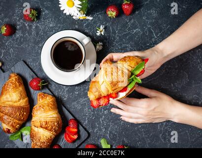 Petit déjeuner savoureux. Les mains des femmes contiennent des croissants frais avec des fraises sur fond de pierre noire. Vue de dessus Banque D'Images