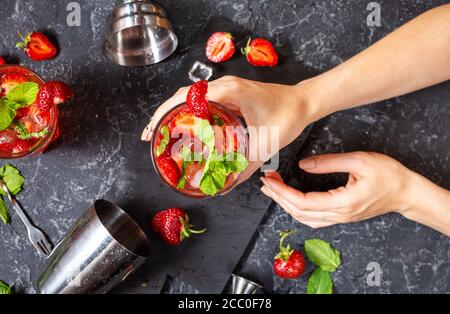 Les mains des femmes ont un verre de mojito de fraise sur fond de pierre noire. Vue de dessus Banque D'Images