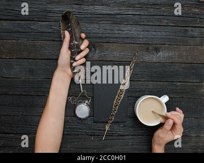 Plume et tasse de café dans une main et un cahier féminins. Ancienne table en bois. Vue de dessus Banque D'Images