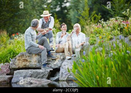 Les aînés satisfaits s'assoient dans le jardin avec un verre de vin blanc en été Banque D'Images