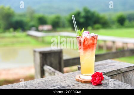 Thé glacé avec une rose de thé cocktail froid / thé fleurs faites de pétales de rose de thé dans un verre table en bois et fond vert naturel Banque D'Images