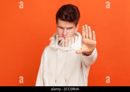 Non ! Un jeune homme plein d'assurance en sweat-shirt décontracté avec un visage sérieux montrant un geste d'arrêt avec sa paume, un adolescent contre l'intimidation et la violence. Goujon intérieur Banque D'Images