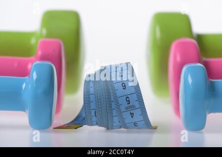 Le régime de santé et les symboles de condition physique. Mode de vie sain et concept sportif. Haltères en plastique bleu, rose et vert sur fond blanc, gros plan. Les cloches sont placées dans le motif près du rouleau de ruban de mesure Banque D'Images
