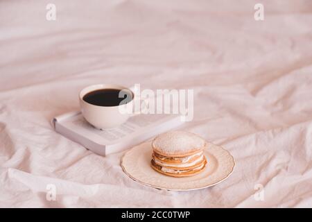 Tasse de café frais sur livre ouvert avec gâteaux de casserole sur plaque blanche dans le lit fermé. Bonjour. Mise au point sélective. Banque D'Images