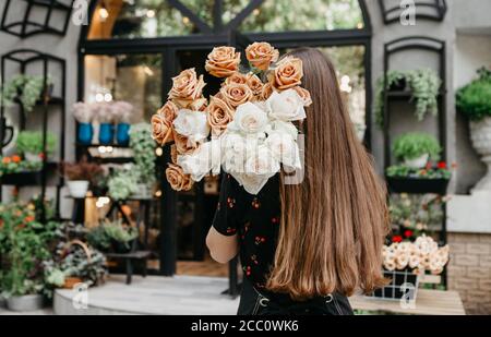 Petite entreprise. Fleuriste en fleuriste, tient des roses blanches et crème sur l'épaule Banque D'Images