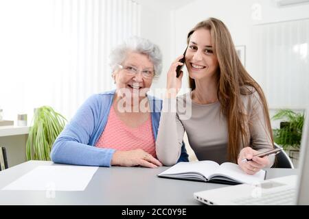 Jeune femme aidant la vieille femme âgée faisant de la paperasserie et administrative procédures avec ordinateur portable à la maison Banque D'Images