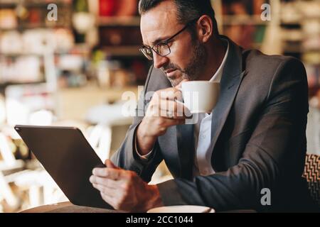 homme d'affaires regardant sa tablette numérique avec une tasse de café à la main au café. homme d'affaires travaillant sur tablette numérique au café Banque D'Images
