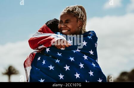 Deux athlètes américains donnent un câlin à un autre après avoir gagné la compétition. Des athlètes féminines enthousiastes s'embrassant avec un drapeau national A. Banque D'Images