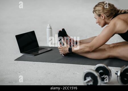 Femme sportive assise sur le sol avec haltères et bouteille d'eau ou de protéines et, à l'aide d'un ordinateur portable Banque D'Images