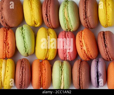 les macarons multicolores cuits ronds se trouvent dans une rangée, plein cadre, gâteau aux amandes brillantes, gros plan Banque D'Images