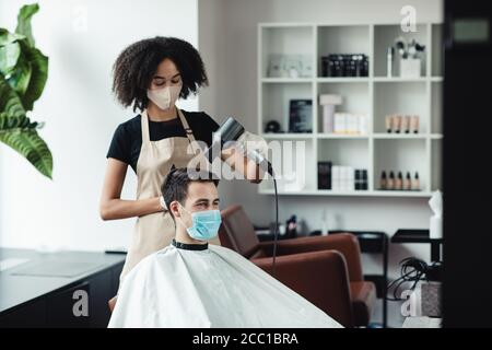 Coiffeur noir faisant une nouvelle coiffure pour le client, les deux dans les masques de protection Banque D'Images