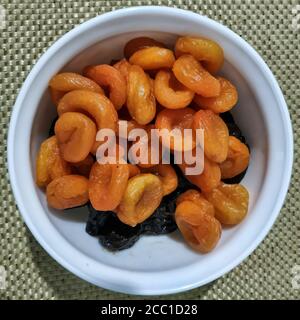 Dans un bol en céramique blanc, fruits séchés - pruneaux et abricots séchés sur le dessus. Vue de dessus Banque D'Images