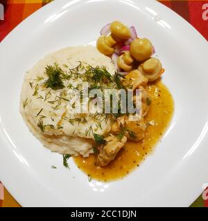 Sur une grande assiette blanche, écrasées de pommes de terre saupoudrées d'aneth vert, à côté de morceaux de dinde compotée avec sauce et de champignons marinés avec des oignons Banque D'Images