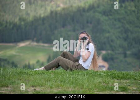 Fille avec l'appareil photo est assis sur une colline et des photos. Forêt en arrière-plan Banque D'Images