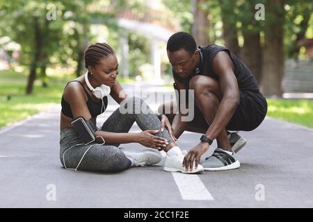 Blessures par jogging. Black Guy aidant petite amie souffrant de la cheville tentaculaire après la course Banque D'Images