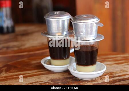 Café traditionnel du Vietnam avec lait condensé sucré sur fond de table en bois. Café noir goutte dans le style vietnamien . Banque D'Images
