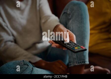 Gros plan de la main jeune femme tenant la télécommande et changeant chaîne à la maison regardant la télévision seule Banque D'Images