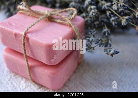 Deux barres de savon artisanal rose nouées avec des fleurs de ficelle et de lavande sur fond de bois blanc. Mise au point sélective, espace de copie Banque D'Images