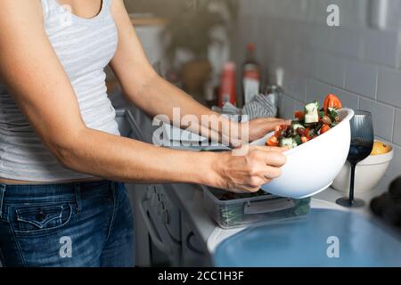 Une femme fait de la salade dans une cuisine, mélangeant des légumes avec des épices dans un bol Banque D'Images