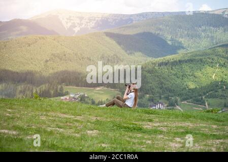 Une fille avec un appareil photo est assise sur une colline et des photos de montagne. Jour d'été Banque D'Images