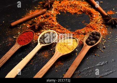 Cuillères à bois avec paprika, curcuma, herbes et poivre à la cannelle et à l'anis. Composition du condiment en forme de coeur. Concept de l'art alimentaire. Ensemble d'épices sur fond de texture gris foncé. Banque D'Images