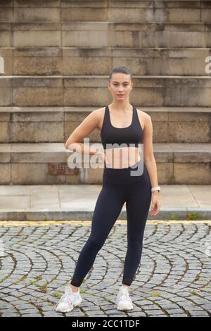 Une jeune femme sportive portant des vêtements de sport debout devant un ensemble de marches, prête pour l'exercice. Banque D'Images