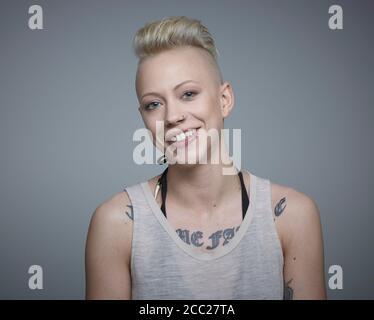 Portrait de jeune femme avec des tatouages à l'arrière-plan gris, smiling Banque D'Images