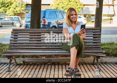 Une jeune femme regarde son téléphone assis sur un banc Banque D'Images