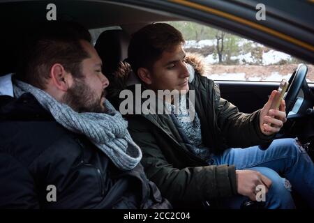Deux jeunes hommes regardent un téléphone à l'intérieur d'une voiture. Concept de recherche d'itinéraire Banque D'Images