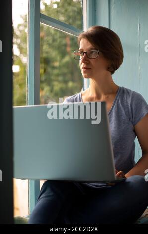 Femme freelance assise sur un rebord de fenêtre travaillant sur un ordinateur portable Banque D'Images