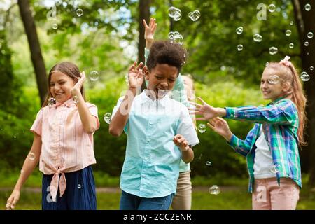 Portrait à la taille du groupe multiethnique d'enfants insouciants jouant avec bulles à l'extérieur dans le parc Banque D'Images