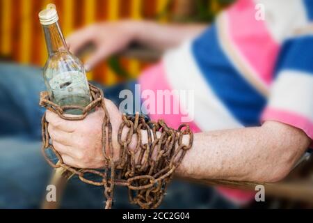 Main enchaînée à une bouteille d'alcool, un homme assis dans une chaise Banque D'Images