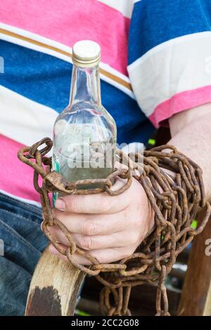 Main enchaînée à une bouteille d'alcool, un homme assis dans une chaise Banque D'Images