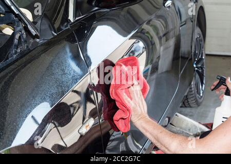 Un homme de nettoyage de voiture avec un chiffon en microfibre, des détails de voiture ou un concept de valeting. Banque D'Images