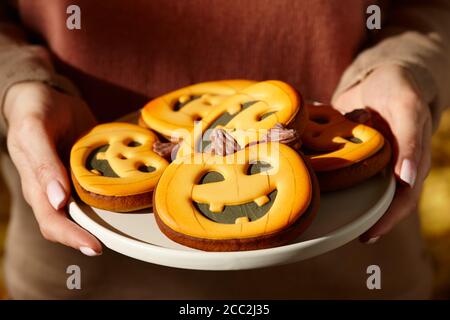 Femme tenant des citrouilles de pain d'épice d'halloween dans une assiette, bonbons de vacances Banque D'Images