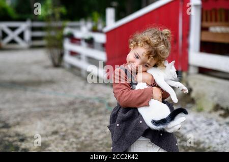 Petite fille avec chat debout à la ferme, jouant. Banque D'Images