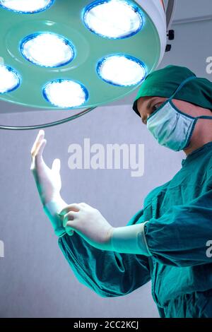 Chirurgien professionnel médecin préparant et portant des gants chirurgicaux sur les mains avant la chirurgie dans la salle d'opération des urgences de l'hôpital. Banque D'Images