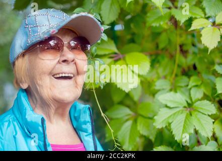 Une grand-mère de 90 ans à la mode et heureuse avec des cheveux gris, des lunettes de soleil et un sourire dans la nature, le temps d'un soleil d'été. Banque D'Images