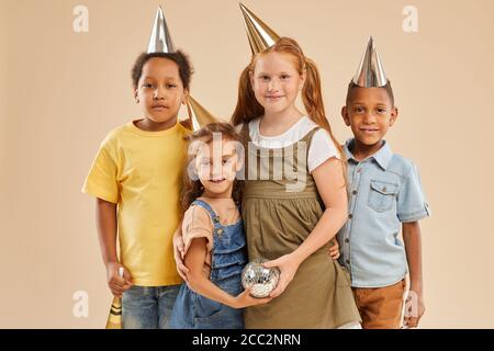 Portrait à taille haute de divers groupes d'enfants portant la fête chapeaux regardant l'appareil photo tout en se tenant contre un fond uni à l'intérieur studio Banque D'Images