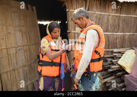 Une femme et son mari ont enfilé des gilets de sauvetage dans un exercice de préparation aux inondations à l'extérieur de leur maison dans le district de Champaran Ouest, Bihar, Inde. Des gilets de sauvetage sont fournis à leurs communautés et à d’autres communautés susceptibles d’être inondées dans les bassins fluviaux de Gandak et de Koshi le long de la frontière entre le Népal et l’Inde dans le cadre du projet de résilience aux crues transfrontières du LWR. Banque D'Images