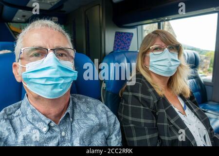 Homme et femme d'âge moyen voyageant dans les transports en commun pendant l'épidémie de Covid-19 au Royaume-Uni, portant des masques chirurgicaux. En regardant la caméra. Banque D'Images