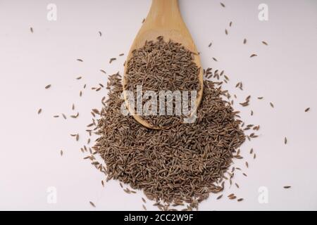 Cuillère en bois pleine de graines de cumin isolées sur fond blanc. Banque D'Images